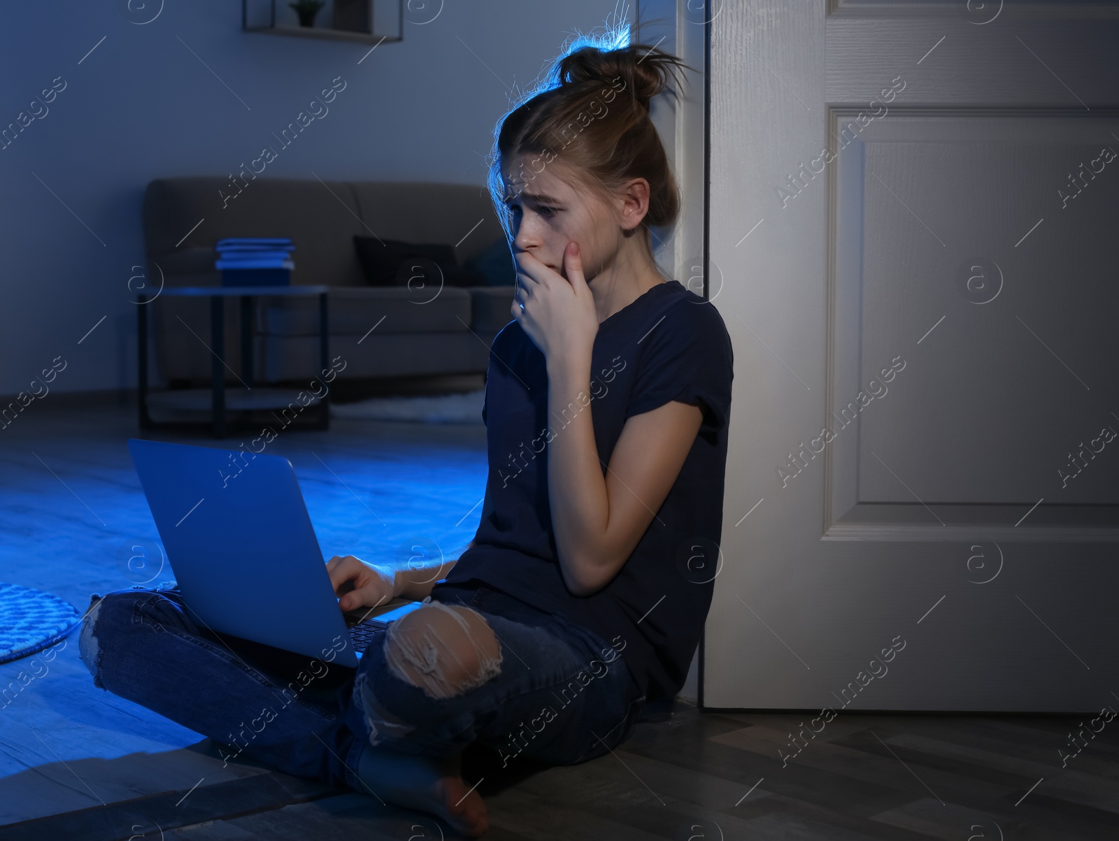 Photo of Terrified teenage girl with laptop on floor in dark room. Danger of internet