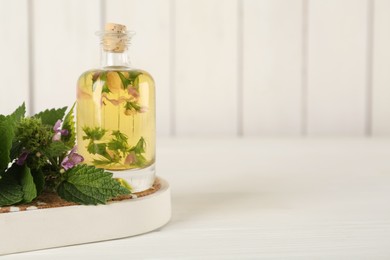 Glass bottle of nettle oil with flowers and leaves on white wooden table. Space for text