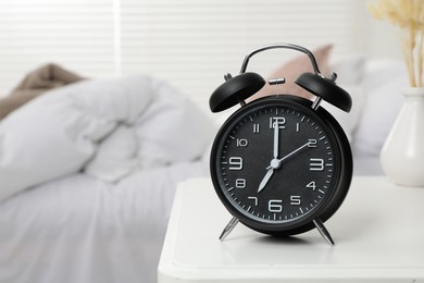 Black alarm clock on white wooden nightstand in bedroom, space for text