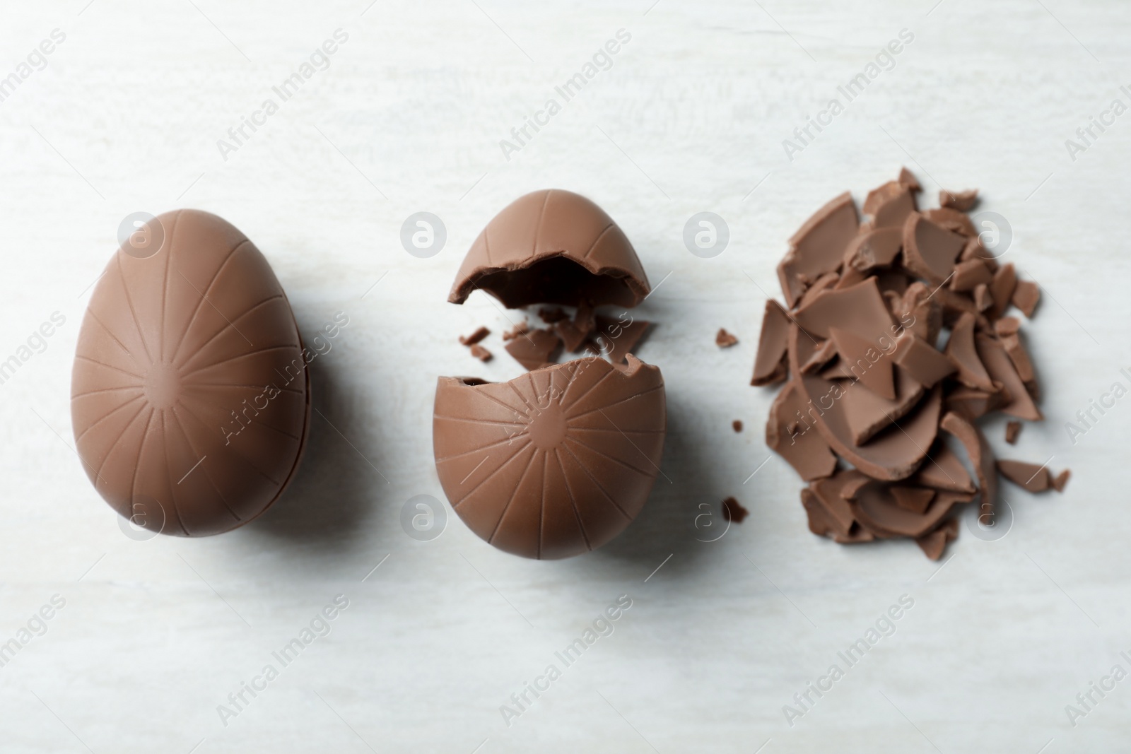 Photo of Broken chocolate eggs on white wooden table, flat lay