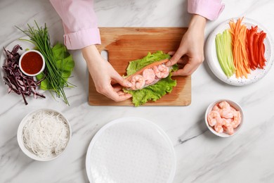 Photo of Woman making delicious spring roll with shrimps at white marble table, top view