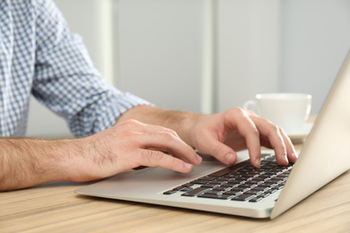 Photo of Man working with modern laptop at wooden table indoors, closeup