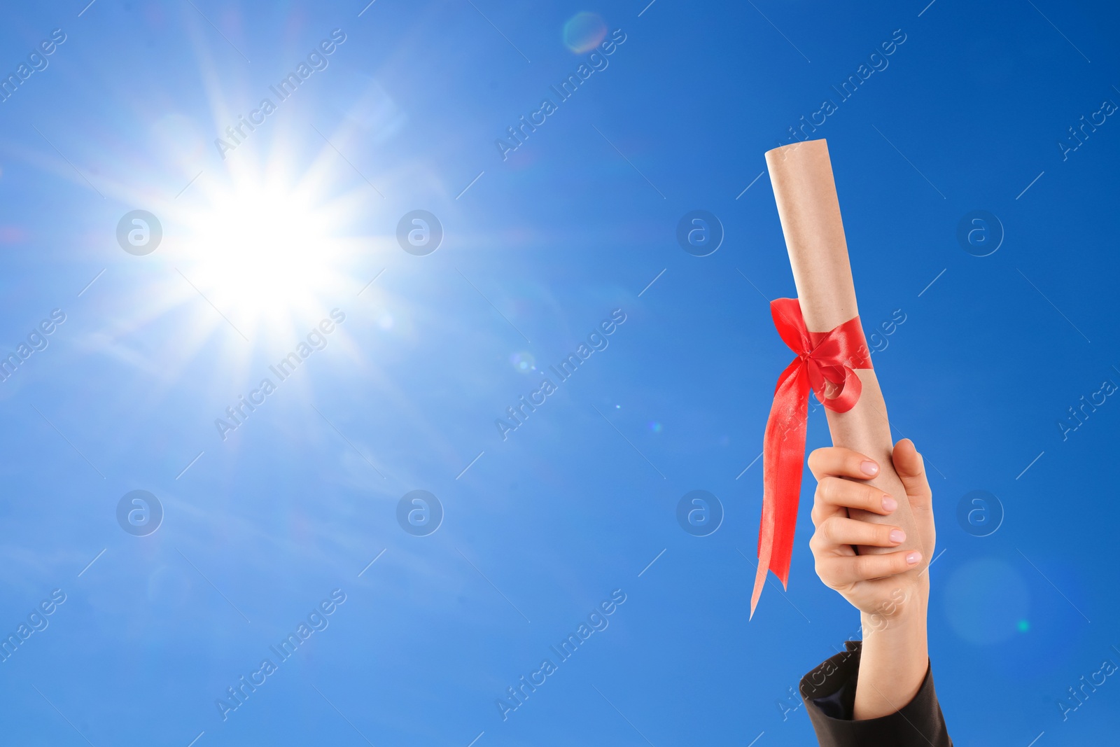 Image of Graduated student holding diploma against blue sky on sunny day, closeup