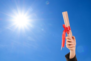 Graduated student holding diploma against blue sky on sunny day, closeup