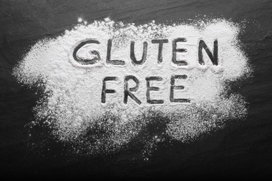 Photo of Phrase Gluten free written with flour on black table, top view