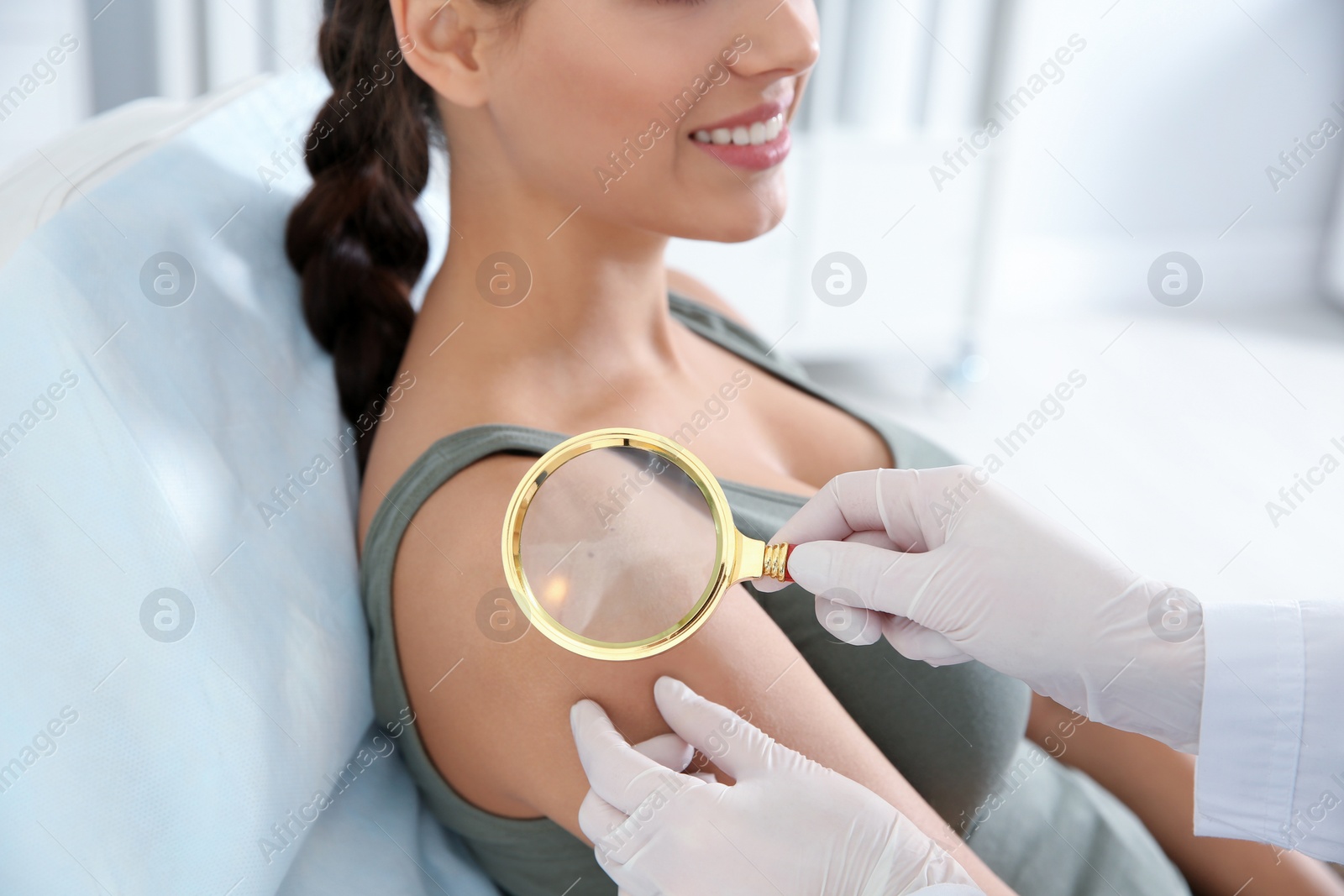 Photo of Dermatologist examining patient's birthmark with magnifying glass in clinic, closeup