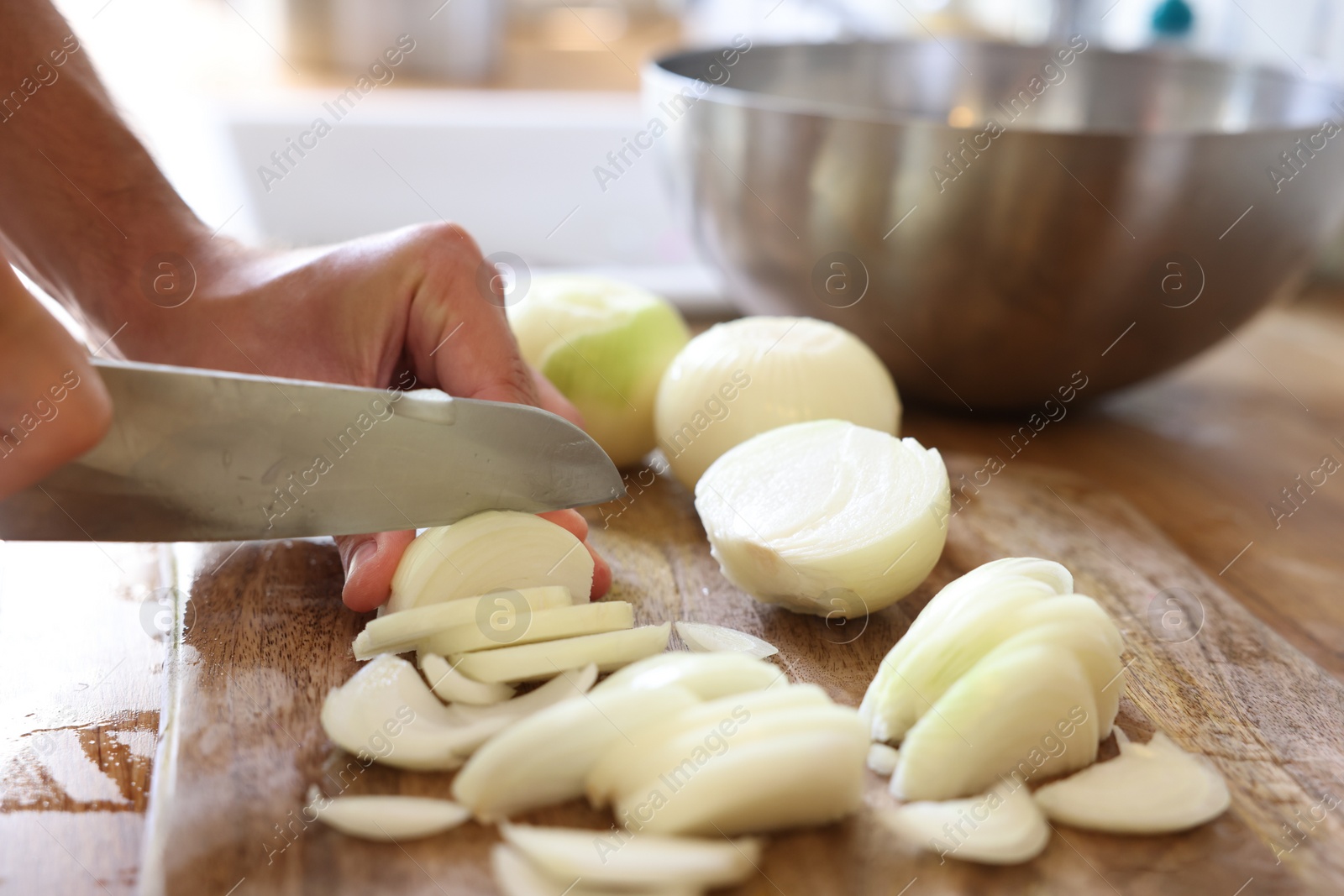 Photo of Woman cutting fresh ripe onion on wooden board, closeup