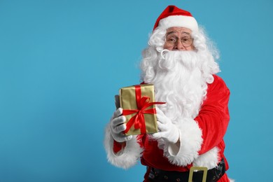 Photo of Santa Claus holding Christmas gift on light blue background, space for text