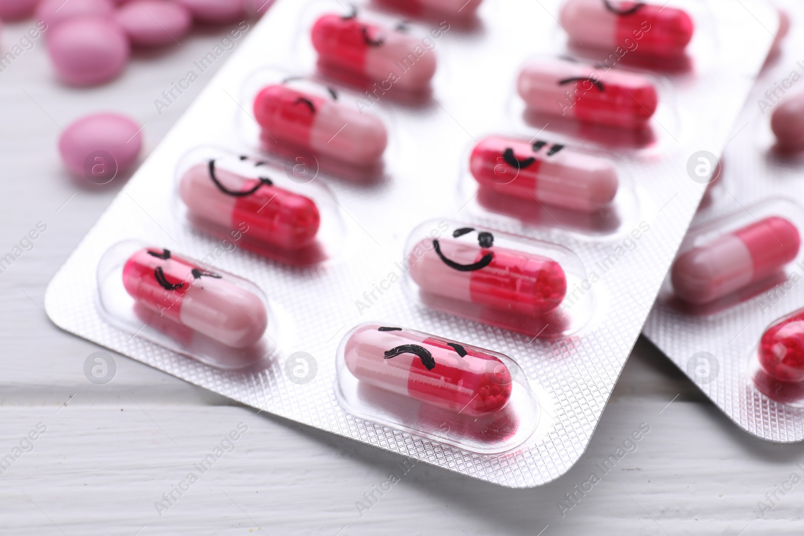 Photo of Blister of antidepressants with different emoticons on white wooden table, closeup