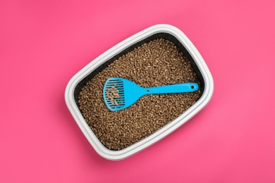 Cat litter tray with filler and scoop on pink background, top view