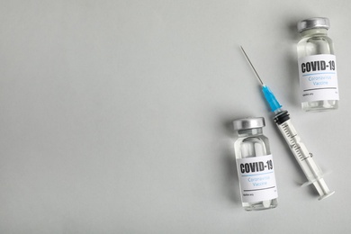 Photo of Vials with coronavirus vaccine and syringe on light background, flat lay. Space for text