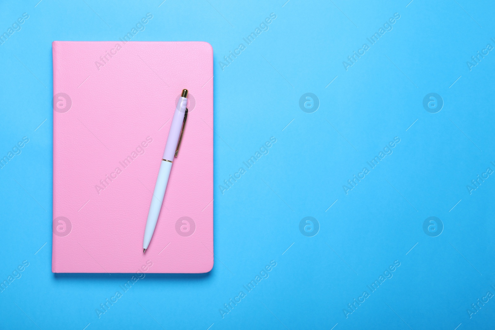 Photo of Closed pink notebook and pen on light blue background, top view. Space for text