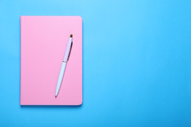 Photo of Closed pink notebook and pen on light blue background, top view. Space for text