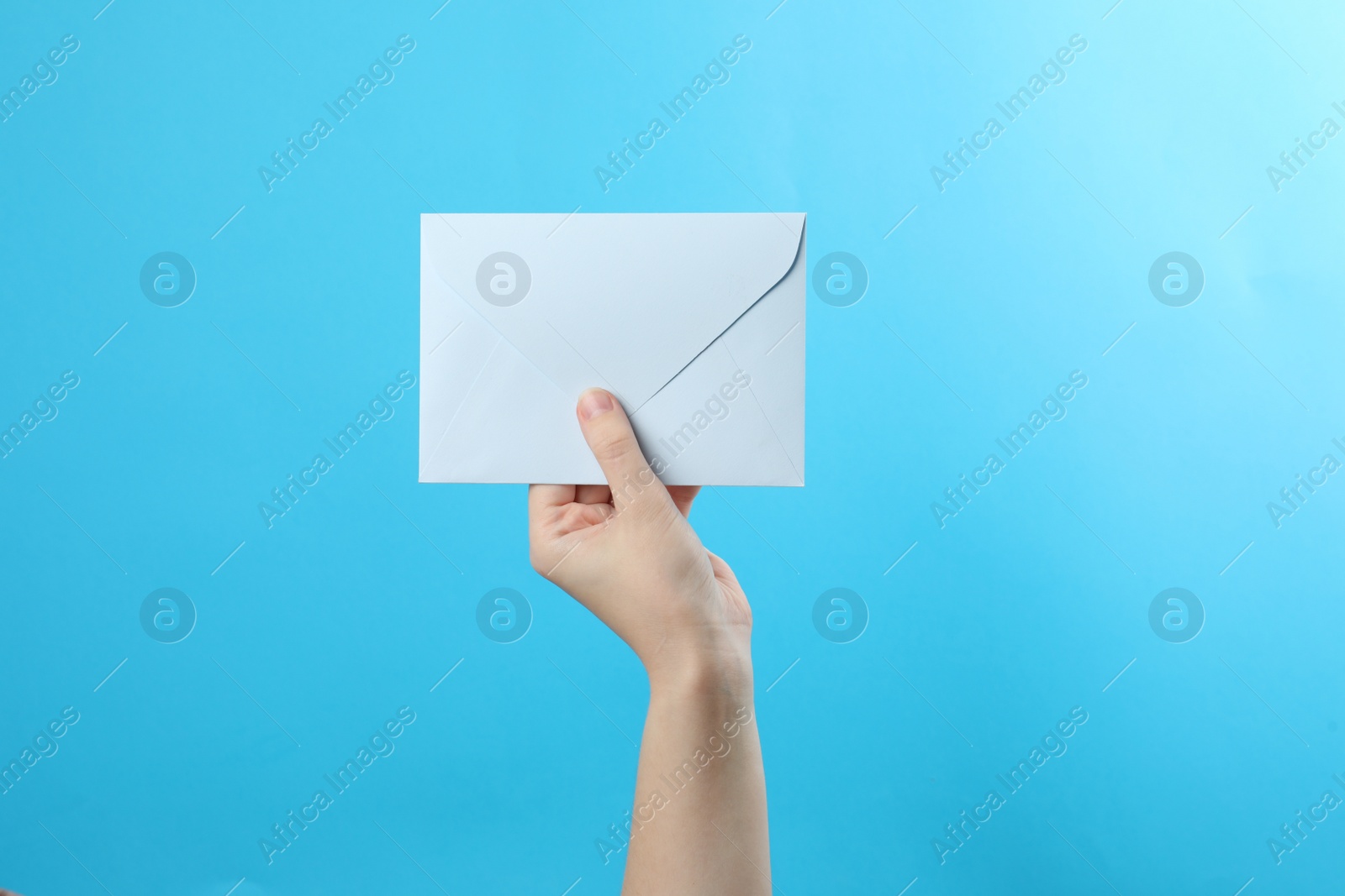 Photo of Woman holding white paper envelope on light blue background, closeup