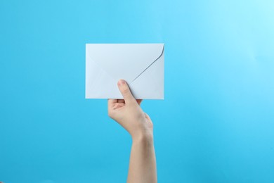 Photo of Woman holding white paper envelope on light blue background, closeup