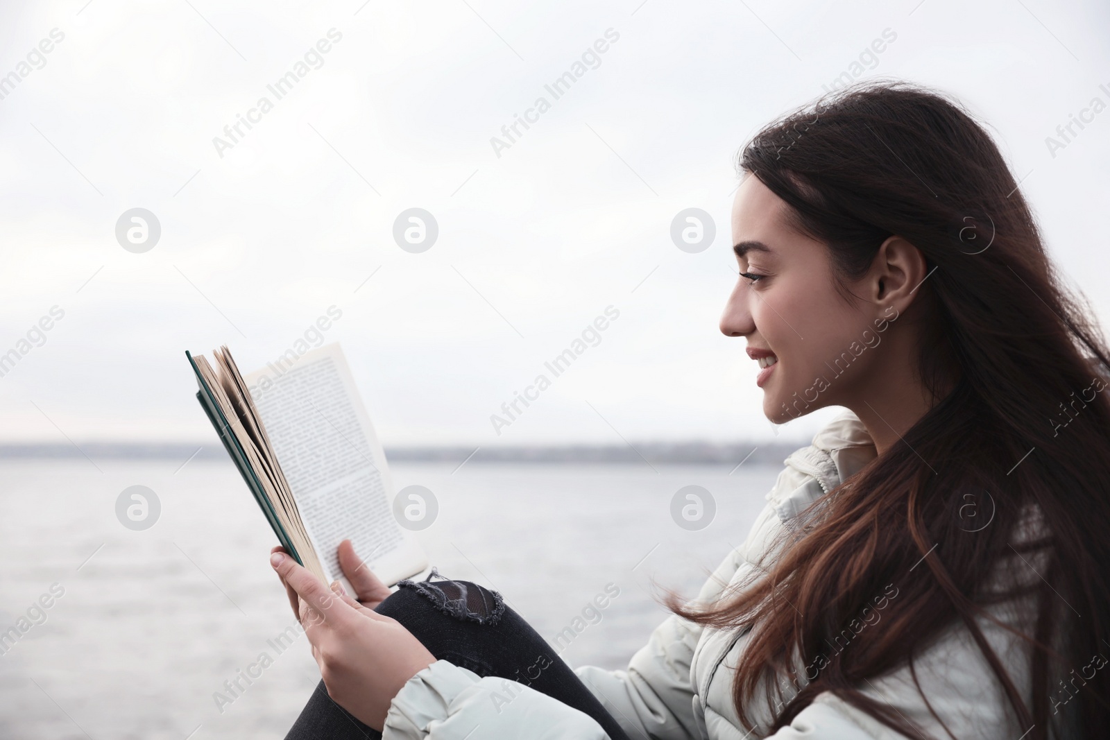 Photo of Woman reading book near river on cloudy day