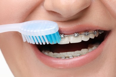 Woman with dental braces cleaning teeth on white background, closeup