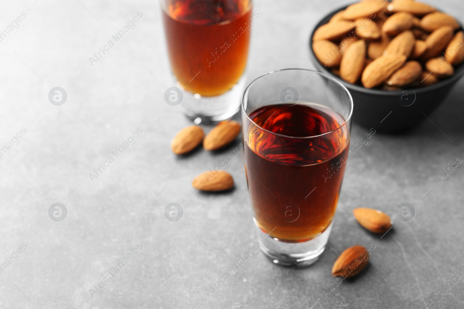 Photo of Glasses with tasty amaretto liqueur and almonds on gray table, closeup. Space for text