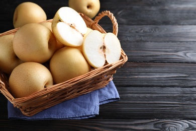Photo of Cut and whole apple pears in basket on black wooden table. Space for text