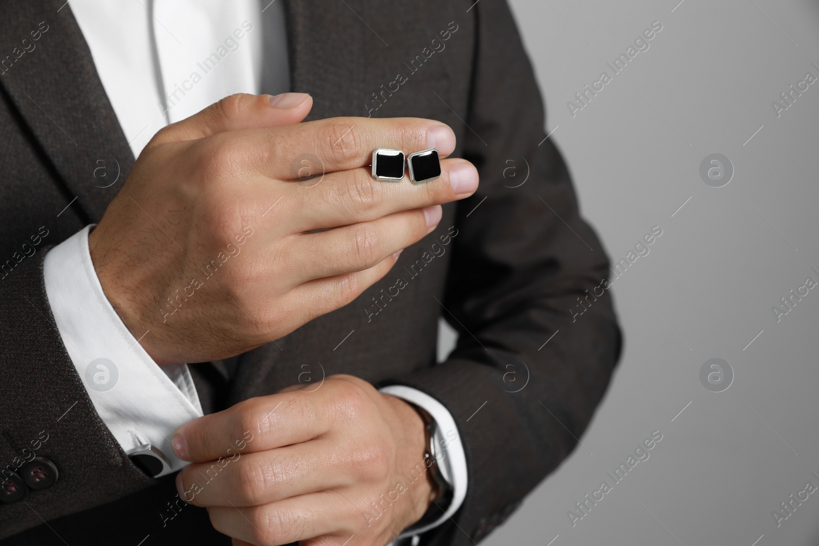 Photo of Stylish man holding cufflinks against grey background, closeup
