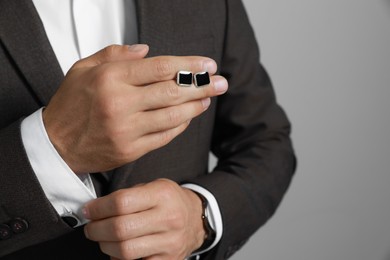 Stylish man holding cufflinks against grey background, closeup