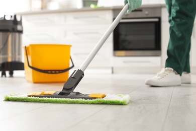 Photo of Professional janitor cleaning floor with mop in kitchen, closeup. Space for text