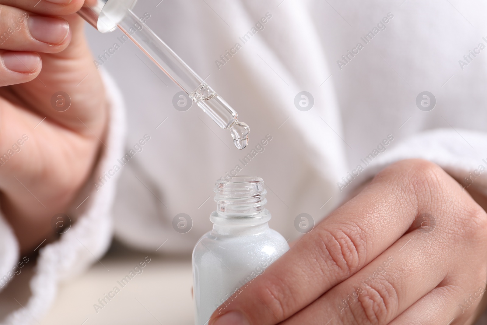 Photo of Woman with bottle of cosmetic serum at table, closeup