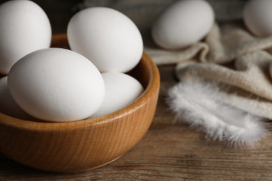 Photo of Many fresh raw chicken eggs in bowl on wooden table, closeup