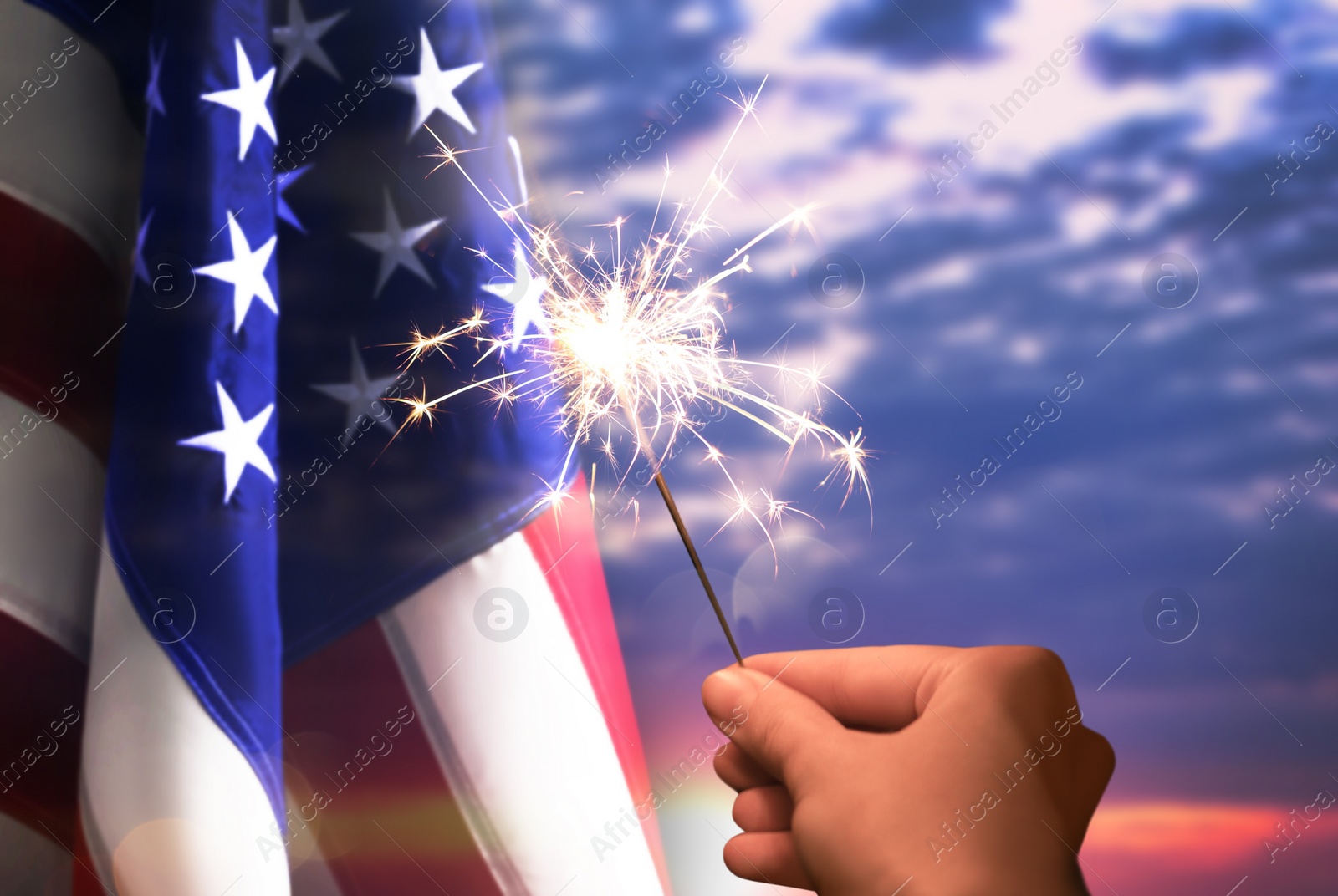 Image of 4th of July - Independence Day of USA. Woman holding burning sparkler near American flag outdoors at sunset, closeup