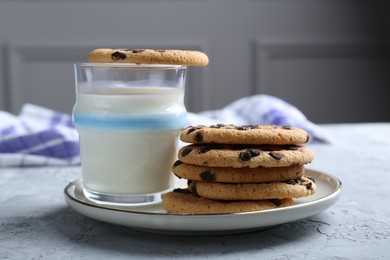 Photo of Delicious chocolate chip cookies and glass of milk on grey textured table