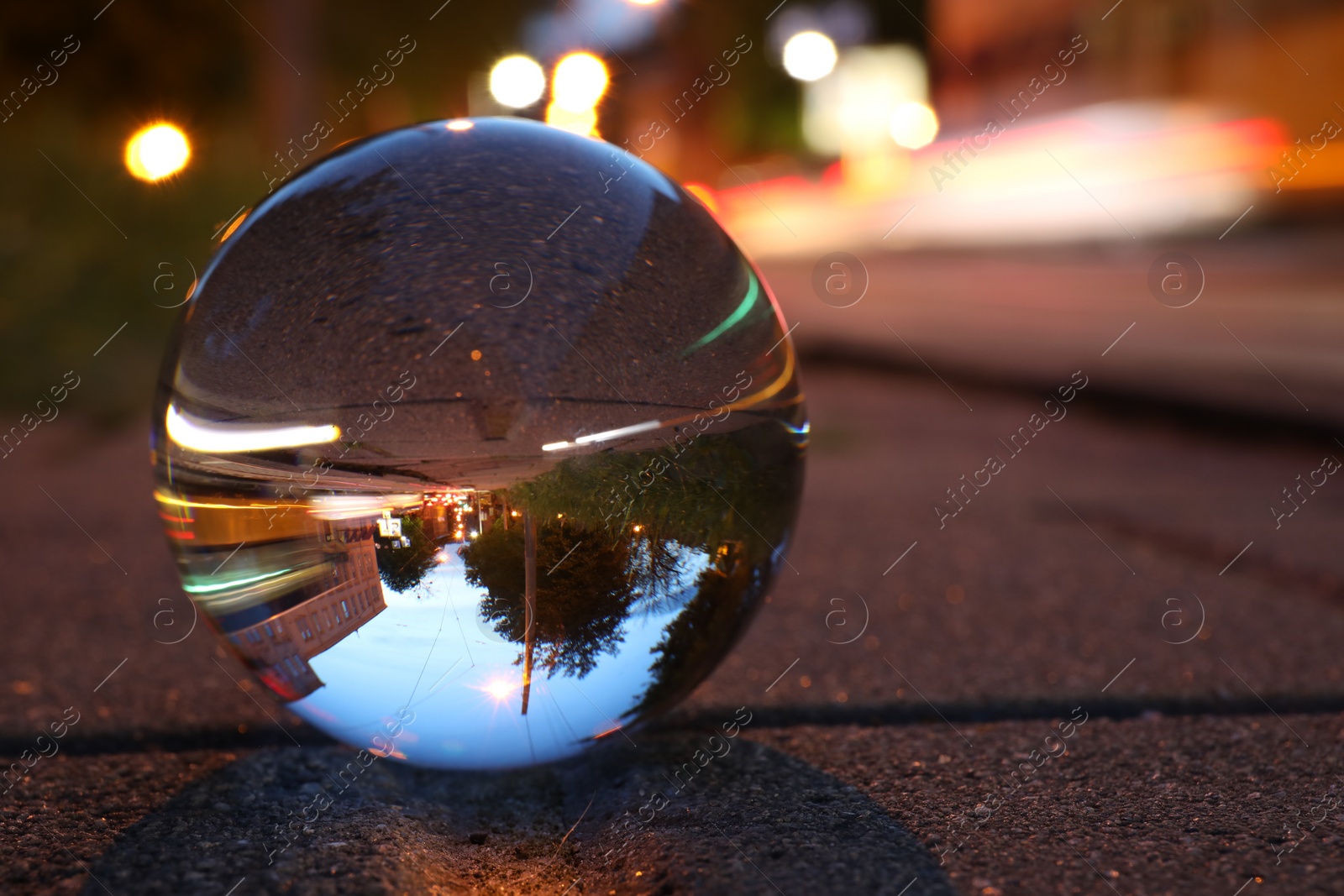 Photo of Beautiful city street, overturned reflection. Crystal ball on asphalt road at night, closeup. Space for text