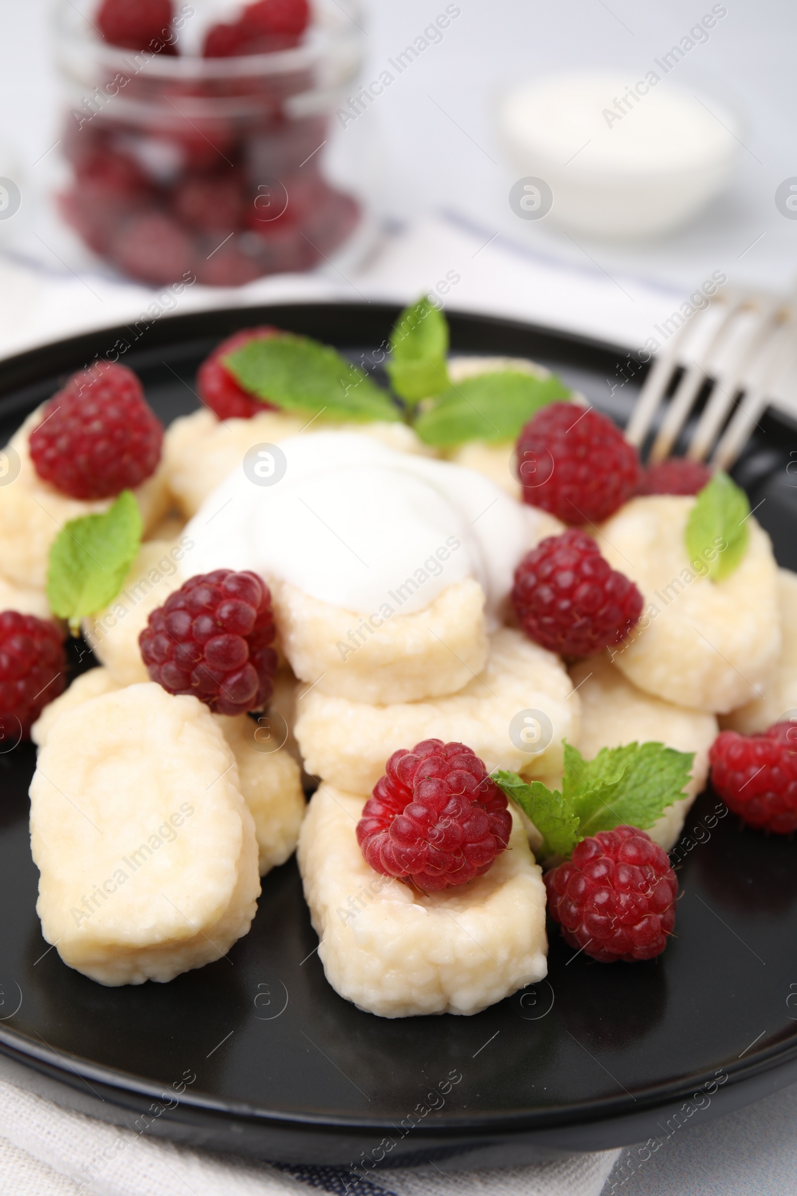 Photo of Plate of tasty lazy dumplings with raspberries, sour cream and mint leaves on table, closeup