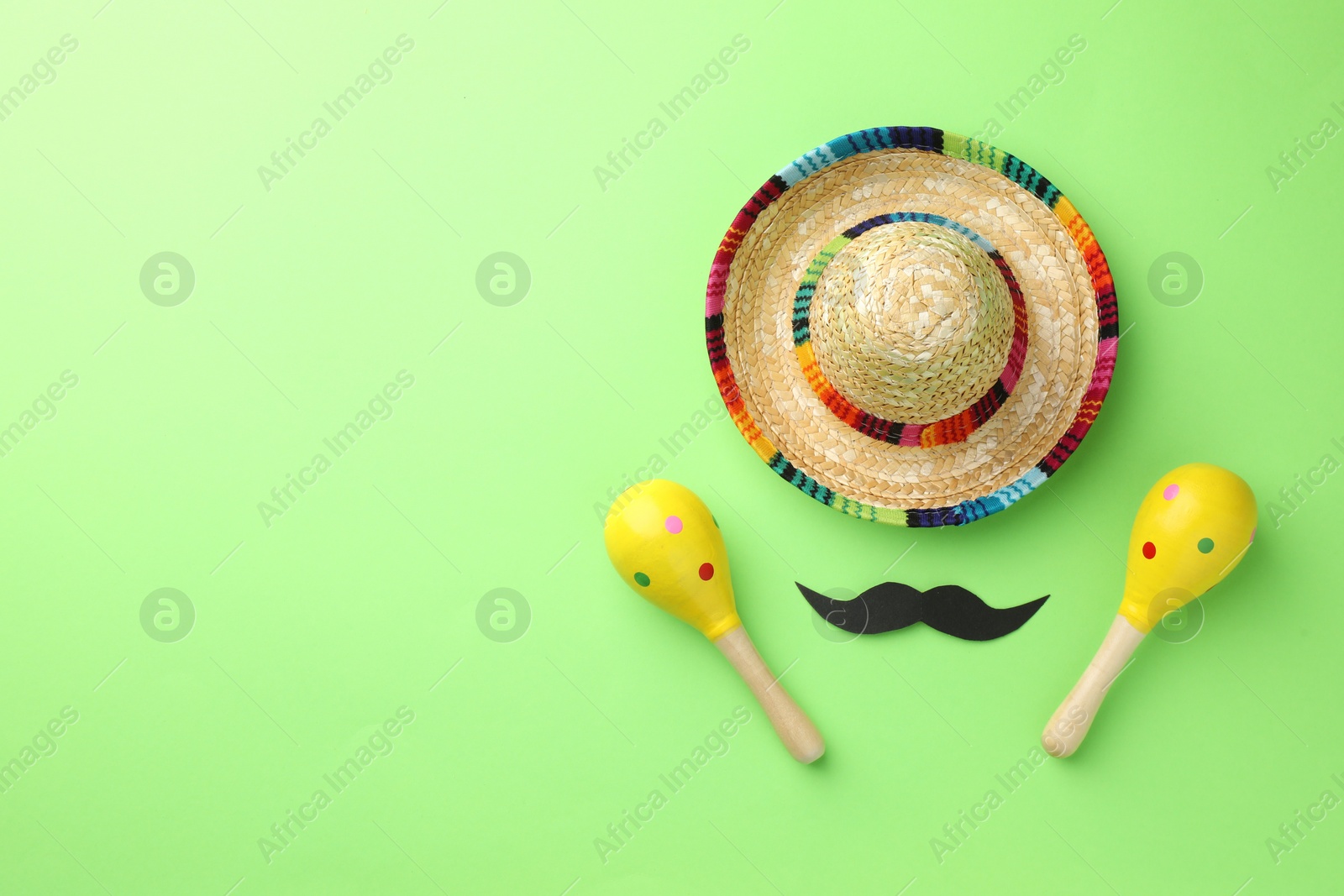 Photo of Mexican sombrero hat, fake mustache and maracas on green background, flat lay. Space for text