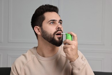 Photo of Young man using throat spray at home