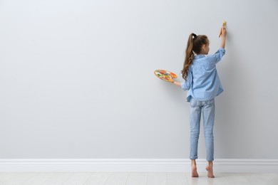 Photo of Little girl painting on light wall indoors, back view. Space for text