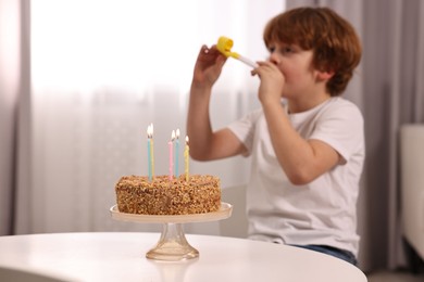 Birthday celebration. Cute boy with party blower at table with tasty cake indoors