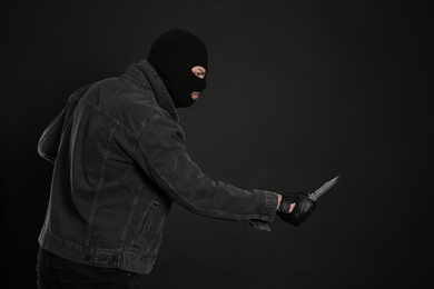 Photo of Man in mask with knife on black background. Dangerous criminal