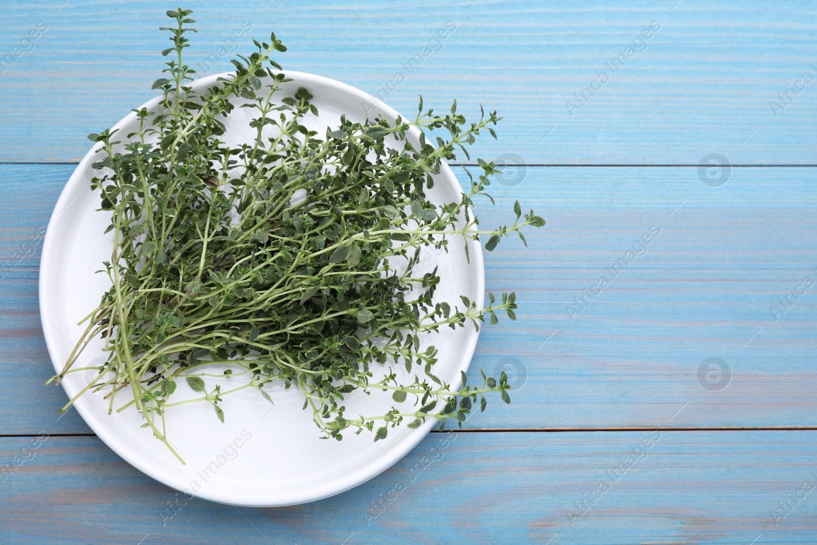 Photo of Bunch of aromatic thyme on light blue wooden table, top view. Space for text