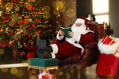 Photo of Santa Claus reading book near decorated Christmas tree indoors