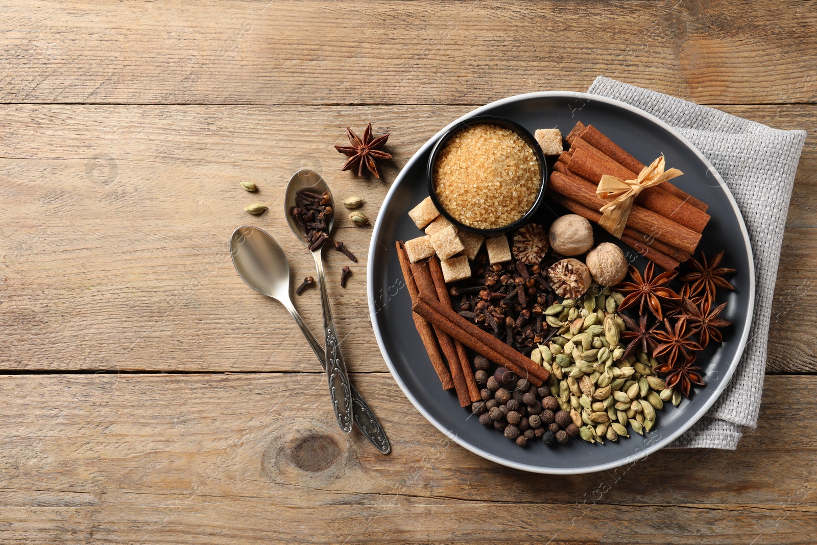 Photo of Plate with different aromatic spices and spoons on wooden table, flat lay. Space for text