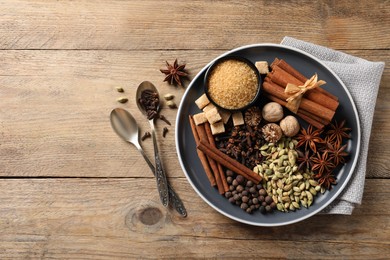 Plate with different aromatic spices and spoons on wooden table, flat lay. Space for text