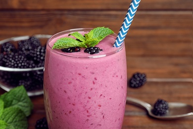 Photo of Glass of blackberry smoothie with straw on table, closeup