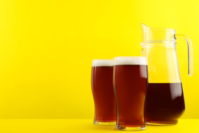 Delicious homemade kvass in glasses and jug on yellow background. Space for text