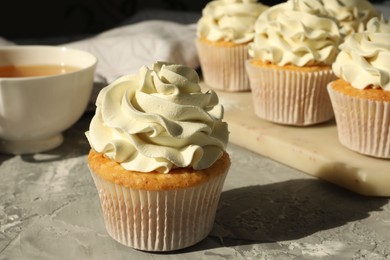 Photo of Tasty cupcakes with vanilla cream on grey table, closeup