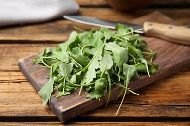 Photo of Cutting board with fresh arugula leaves and knife on wooden table, closeup