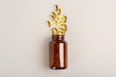 Bottle and vitamin capsules on light grey background, top view