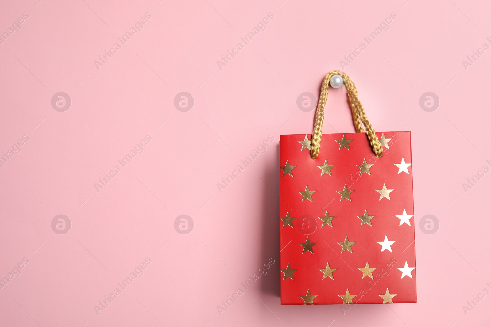 Photo of Red shopping paper bag with star pattern on pink background, space for text