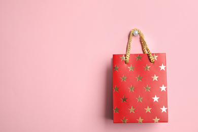 Photo of Red shopping paper bag with star pattern on pink background, space for text