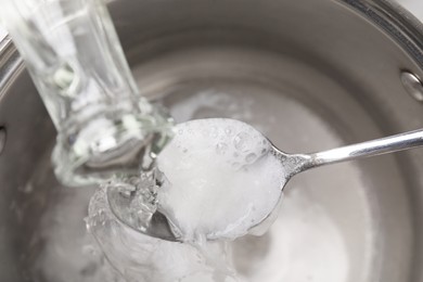 Photo of Pouring vinegar into spoon with baking soda over saucepan, above view