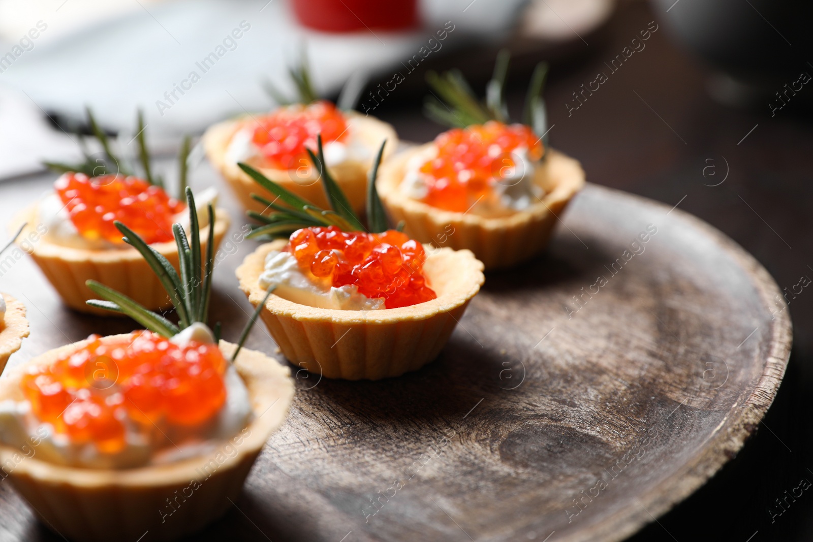 Photo of Delicious tartlets with red caviar and cream cheese served on wooden board, closeup